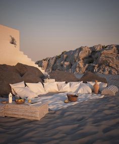 an outdoor seating area on the beach with rocks in the background and food laid out on it