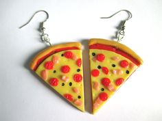 two slices of pizza shaped earrings with cherries hanging from hooks on a white surface