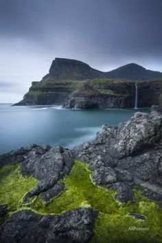 a waterfall is coming out of the water near some rocks and green mossy grass