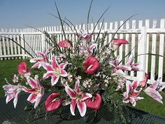 a vase filled with pink and white flowers sitting on top of a table next to a fence