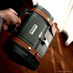 a person holding a green and brown cooler on top of a hard wood floor next to a window