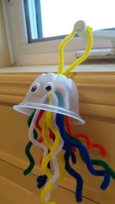 a plastic jellyfish is hanging from the side of a window sill with yellow, blue, green, and red streamers