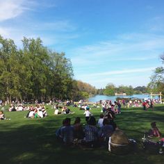 many people are sitting on the grass near water