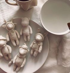 five small stuffed animals on a plate next to a cup and saucer with spoons