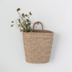 a wicker basket with flowers in it hanging on the wall next to a white wall