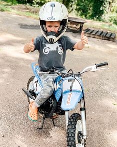 a young boy sitting on top of a dirt bike giving the thumbs up sign while wearing a helmet