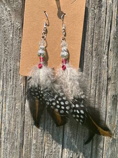 a pair of earrings with feathers hanging from it's ear hooks on a piece of wood