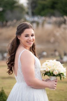 a woman in a white dress holding a bouquet of flowers and smiling at the camera