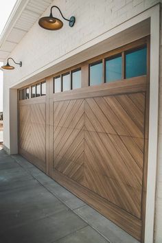 a wooden garage door on the side of a white brick building with two lights above it