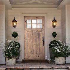 two planters with flowers are in front of a door that is on the side of a house