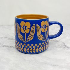 a blue and yellow coffee cup sitting on top of a marble counter next to a white wall