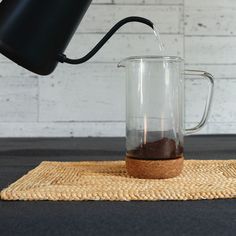 a glass pitcher filled with liquid sitting on top of a mat next to a black lamp