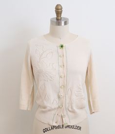 Handmade  1950's/1960's era Vintage Cream/Ivory cotton cardigan with adorable green stitching details. The top button has a cute plastic-like green flower, with others being glass/plastic little globes. Green hand stitching along the seams, and button placket. The body of the cardigan has an intricate floral design is knitted in negative space along the front of the cardigan with a solid knit back. * DETAILS: Era: 1950's/1960's Color: Cream/Ivory/ Green Material: Cotton Closure: Mixed plastic/glass buttons  CONDITION: *Please note two tiny discolorations: one on the back neck and the other on the cuff of sleeve.  MEASUREMENTS: Chest: 36"-42" Waist: 28"- 34" Length: 21" Sleeve: 17" modern size  SMALL/MEDIUM PLEASE NOTE: vintage sizes differ from modern sizes, please do not rely on the vinta Green Cotton Sweater With Button Closure, Cream Cardigan With Buttons For Spring, Cream Cotton Cardigan With Buttons, Vintage Spring Sweater With Buttons, Fitted Green Cotton Cardigan, Cream Cotton Sweater With Button Closure, Green Button-up Cotton Cardigan, Retro Cotton Sweater With Buttons, Vintage Green Cardigan For Spring