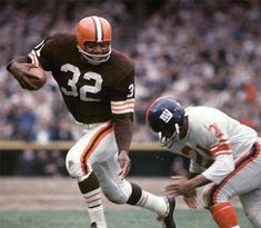 a football player running with the ball in his hand and another person behind him holding an orange and white football