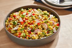 a metal bowl filled with corn and veggies on top of a wooden table