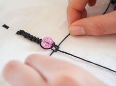 someone is making a beaded bracelet with pink beads and black string on the table