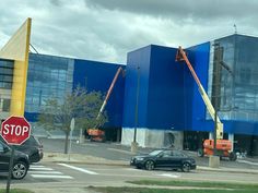 a stop sign in front of a blue building with construction cranes on the side of it