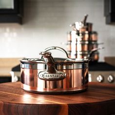 a large copper pot sitting on top of a wooden table next to pots and pans