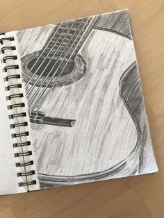 a drawing of an acoustic guitar on a wooden table with a pen and paper next to it