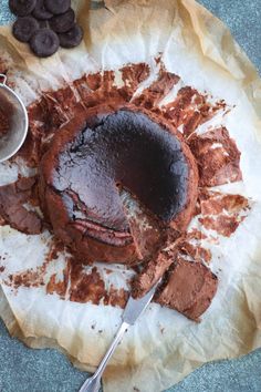 a chocolate cake is cut into pieces and sitting on a piece of parchment paper next to some chocolate chips