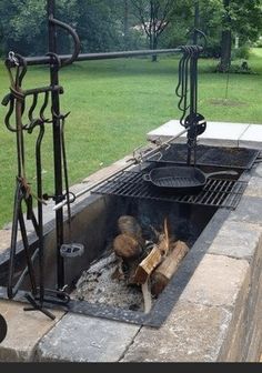 an outdoor fire pit made out of concrete blocks and steel bars with grilling tools on top