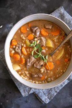 beef barley soup in a white bowl with carrots and parsley