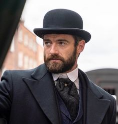 a man with a beard wearing a top hat and suit standing in front of a train