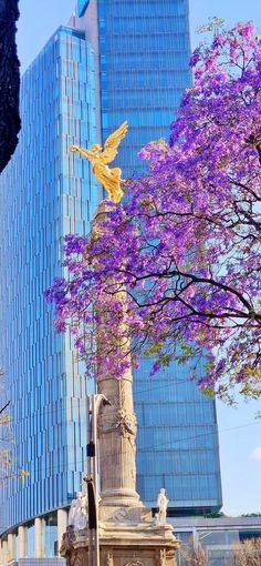 an angel statue in front of a tall building with purple flowers growing on it's side