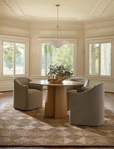 a round dining table surrounded by chairs in a room with large windows and wooden flooring