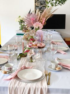 the table is set with plates, silverware and pink napkins