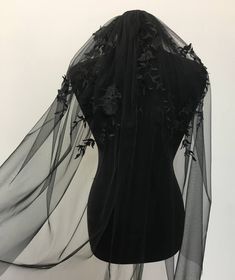 the back of a black dress with flowers and leaves on it, draped over by sheer fabric