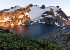 a large mountain with snow on it and some water in the foreground at sunset