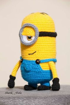 a crocheted minion sitting on top of a gray surface next to a white wall