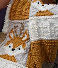 a crocheted blanket with animals on it sitting next to a pillow and chair