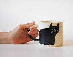 a hand holding a coffee mug with a black cat on it