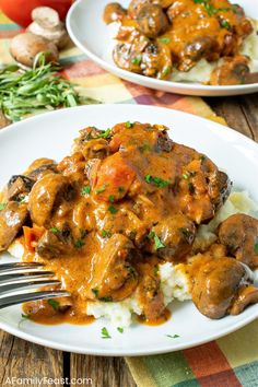 two white plates topped with meat covered in gravy and mashed potatoes on top of a wooden table