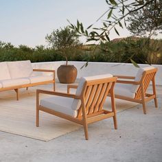 an outdoor seating area with white cushions and wooden furniture on a rug in the foreground