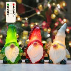 three colorful glass gnomes sitting in front of a christmas tree with lights on it