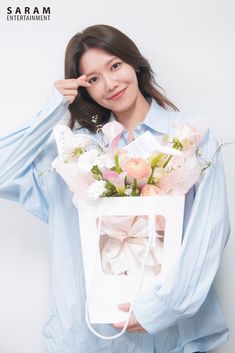 a woman is holding a bag with flowers in it and posing for the camera while wearing a blue shirt