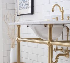 a bathroom with two sinks and gold faucets on the wall above it is white tile