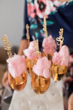 three champagne flutes with pink flowers in them on a table next to a woman's hand