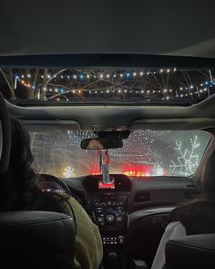 two people driving in the back seat of a car at night with christmas lights behind them