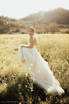 a woman in a wedding dress walking through a field