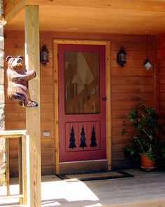 a bear statue on the front porch of a cabin with red door and pine trees