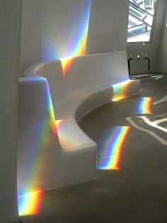 a white couch sitting in the middle of a room with rainbow colored light coming through it