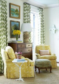 a living room with yellow chairs and green curtains on the window sill, an ottoman and a lamp