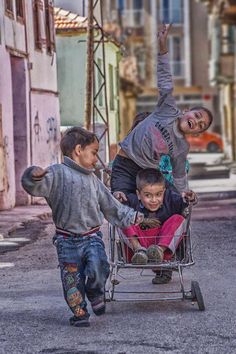 three young boys pushing a shopping cart with one boy in it and the other on his back