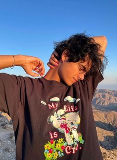 a woman standing on top of a mountain with her hands behind her head and wearing an elephant t - shirt