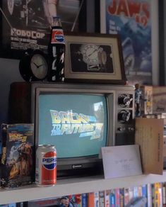 an old tv sitting on top of a book shelf next to a can of soda