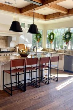 a kitchen with wooden floors and white cabinets, an island table surrounded by four stools